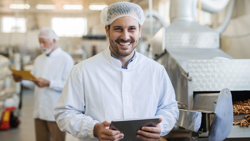 Smiling,Young,Technologist,Using,Tablet.,Food,Factory,Interior.